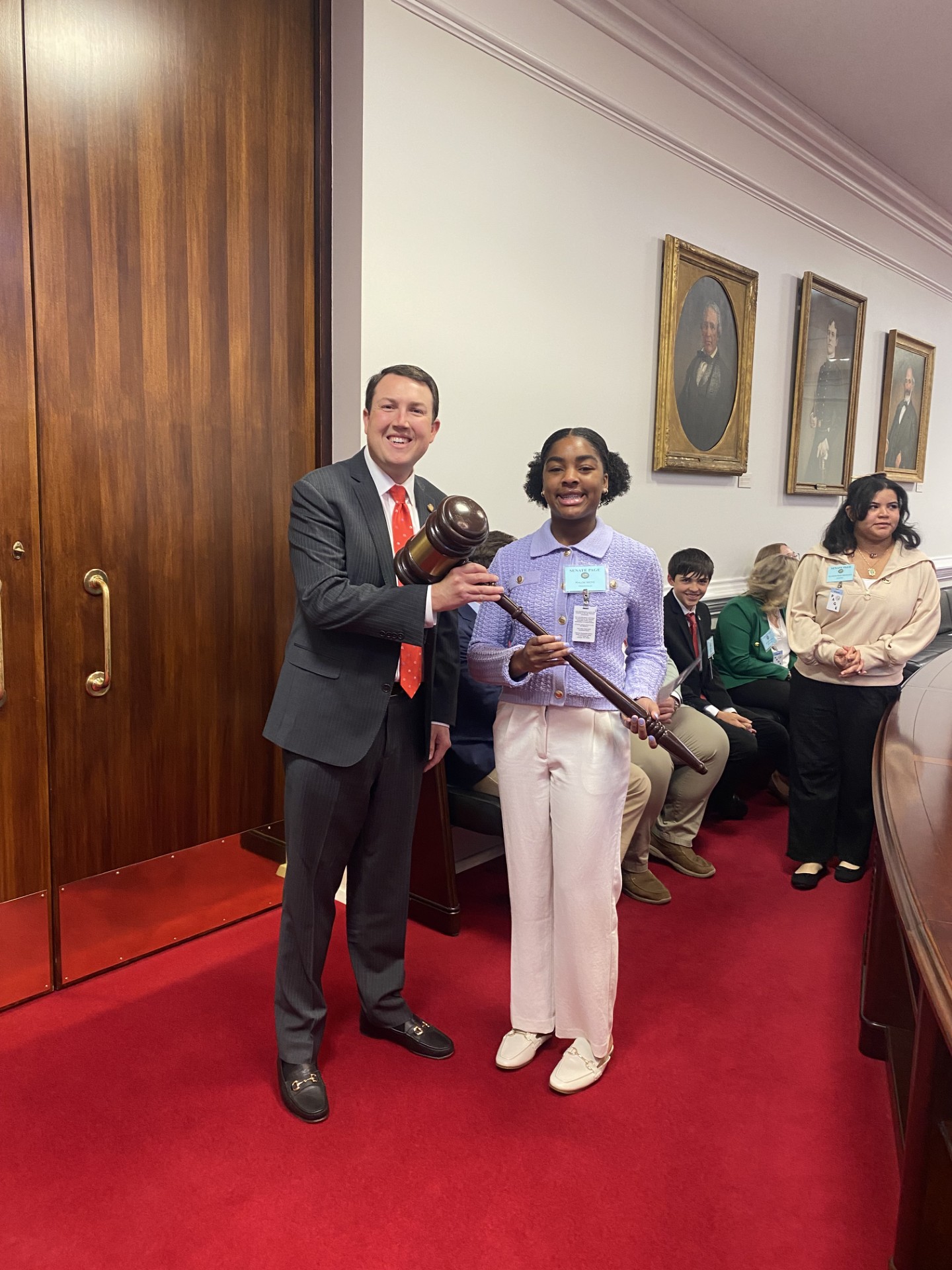 Page posing with a Senator while holding a gavel.